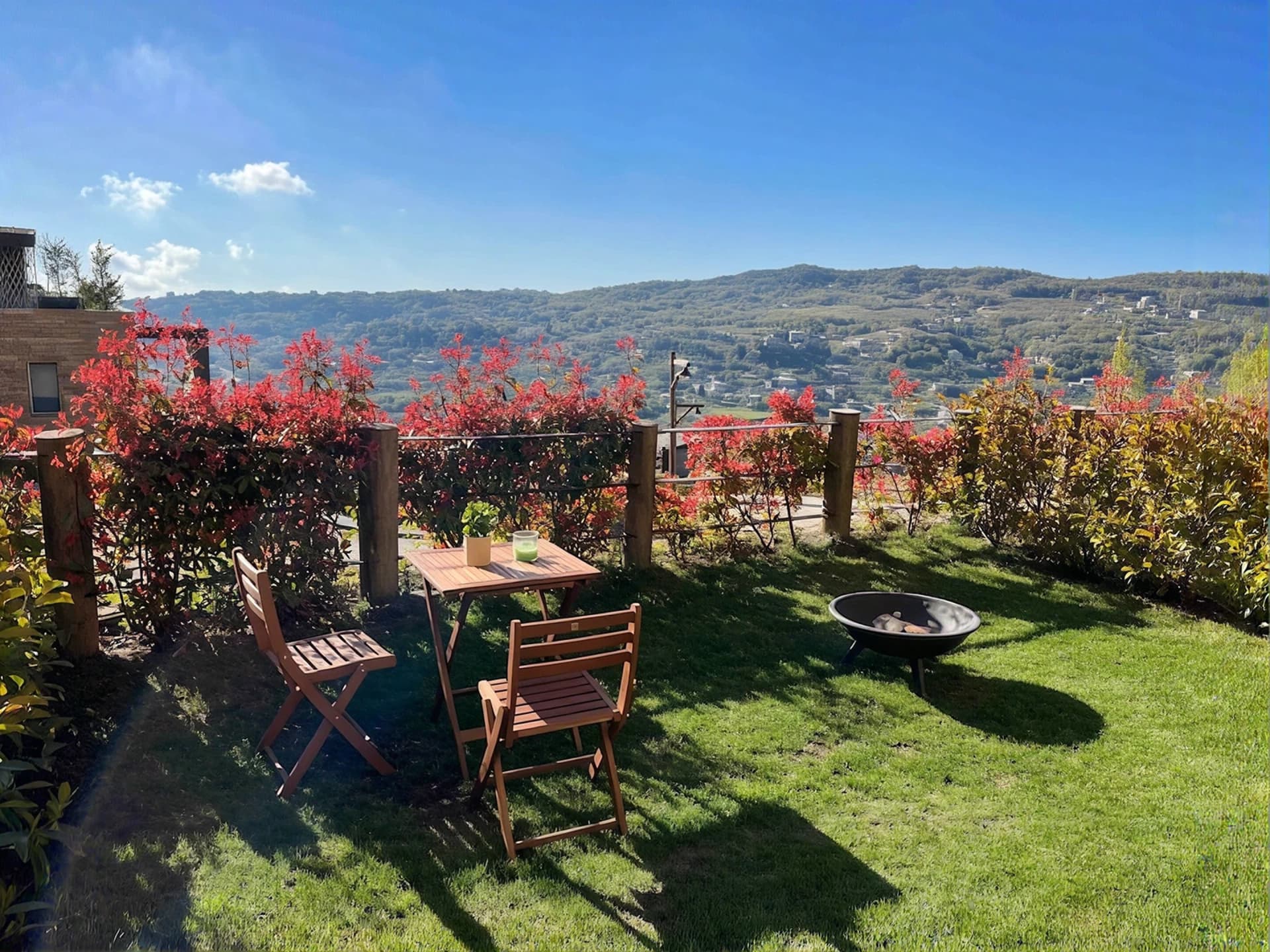 Wooden dining set and fire pit on the private lawn at The Nest, valley views behind
