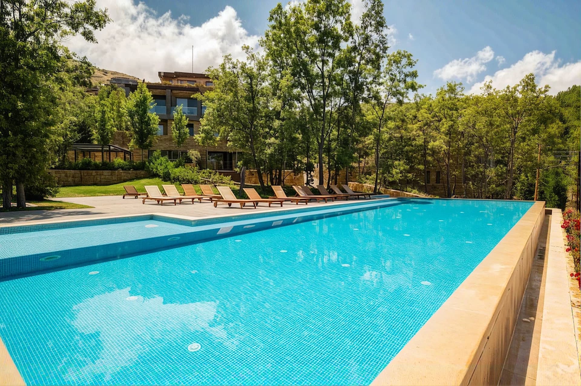 Shared pool with lounge chairs and a stone chalet behind the trees at RedRock